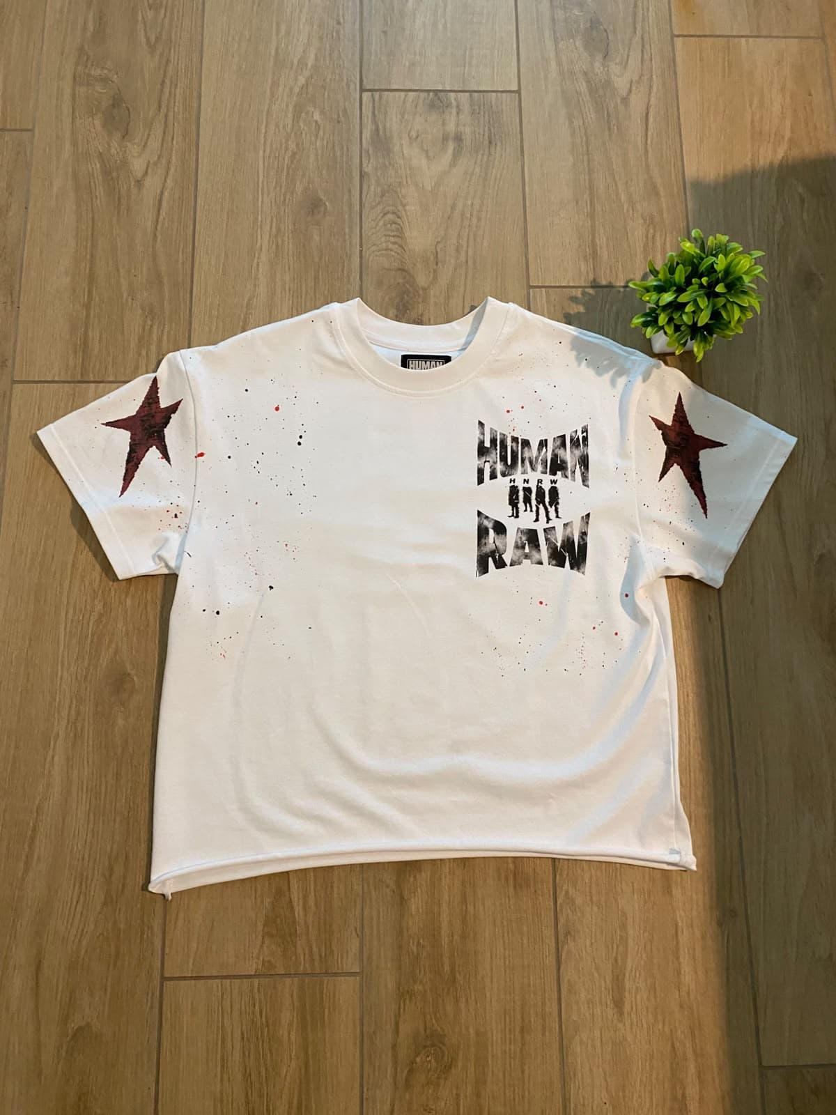 HumanRaw Cropped Tee bianca vista di fronte, stesa su un pavimento in legno